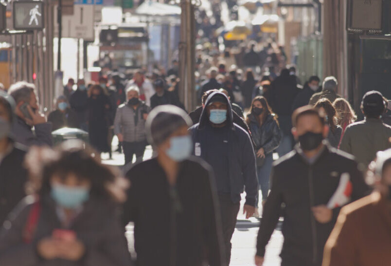 Crowd of people walking street wearing masks